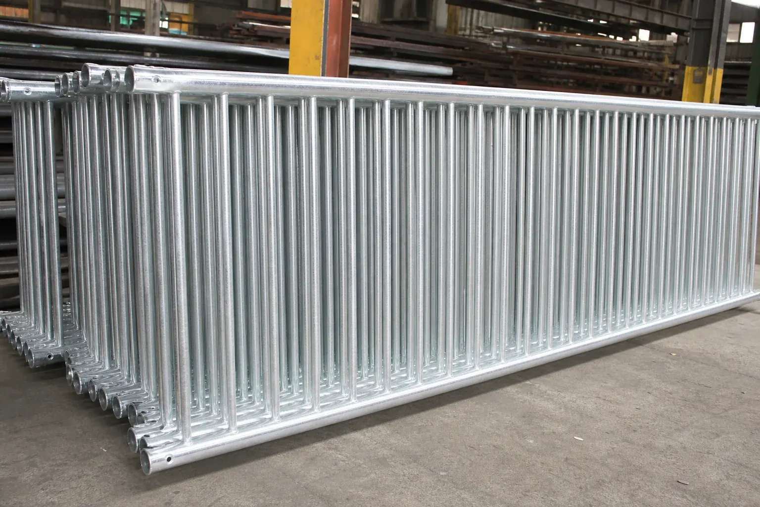 Stacked rigid galvanized steel rod fence panels with a bright zinc finish inside the workshop