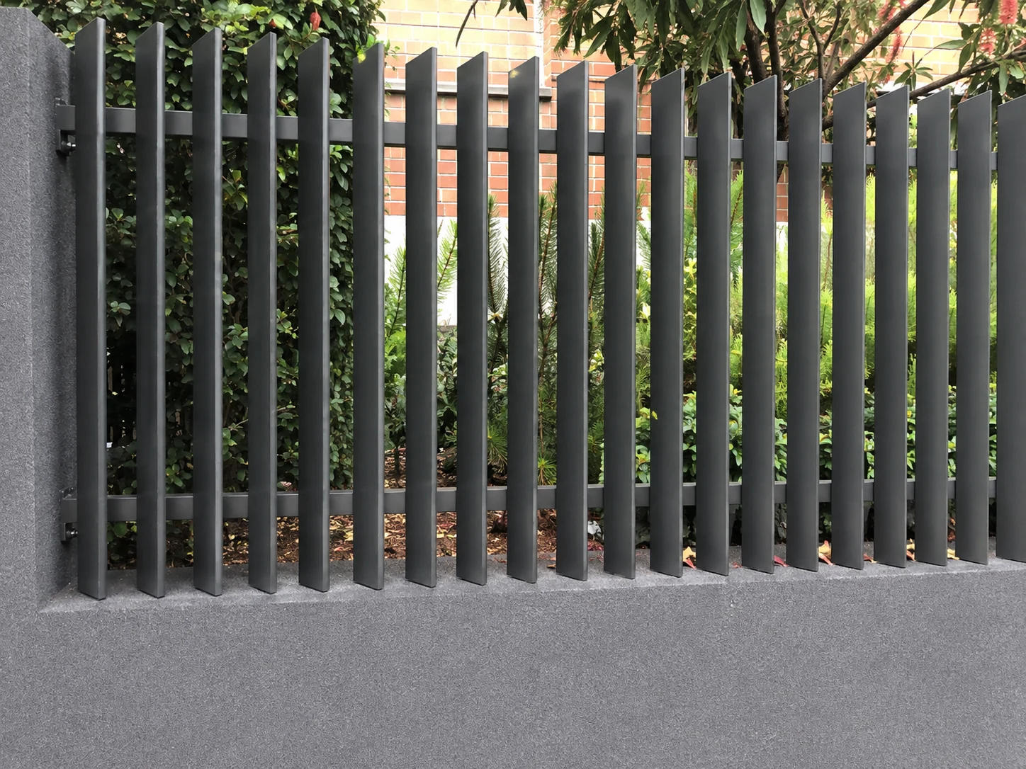 Black vertical 45 degree blade fence panels with offset blades in a landscaped garden