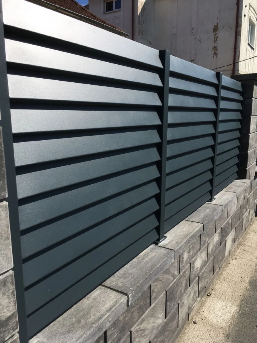 Dark grey horizontal 45 degree blade privacy fence panels mounted on a masonry wall