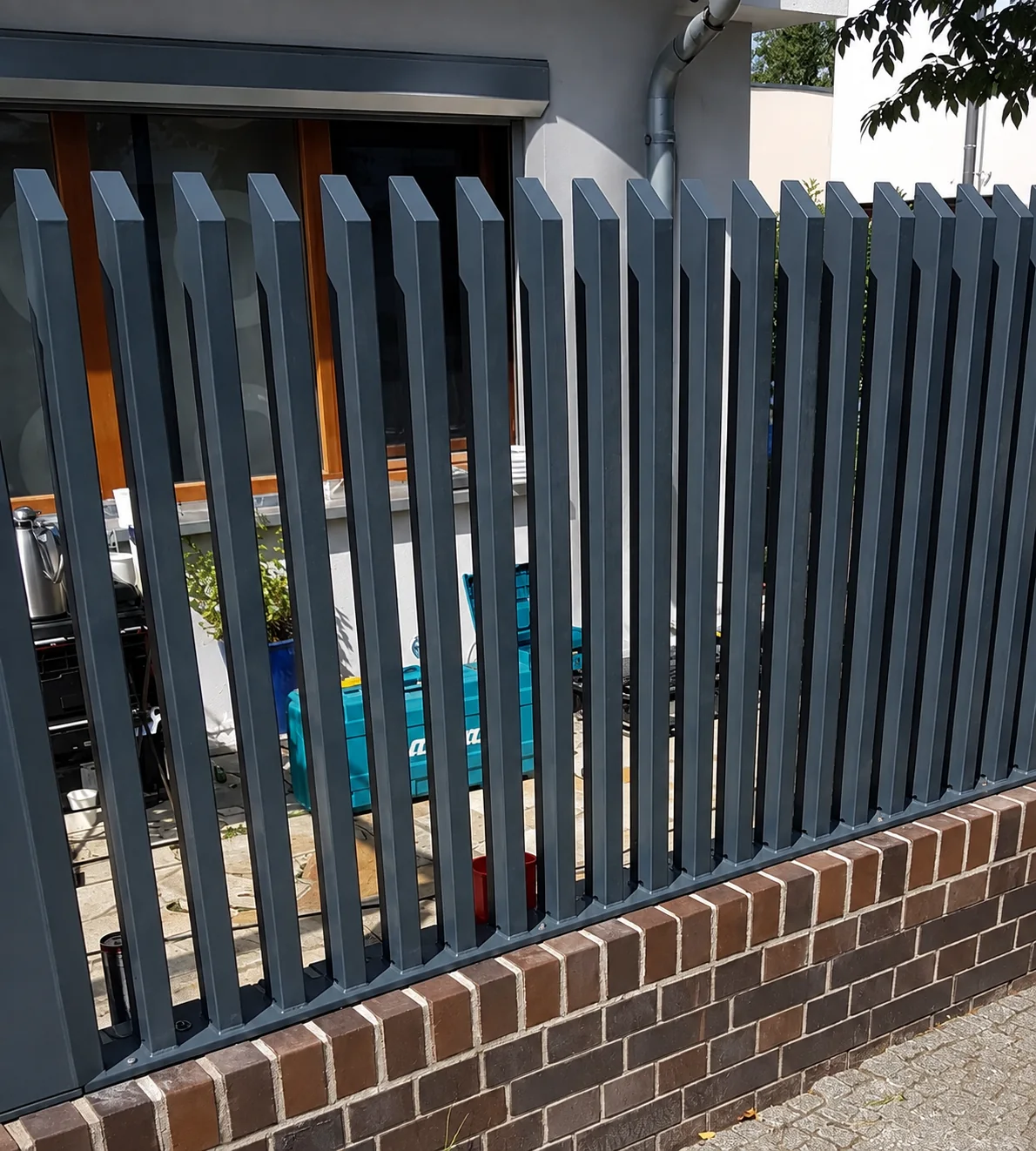Grey aluminium blade fencing with sloped blade tops on a brick boundary wall