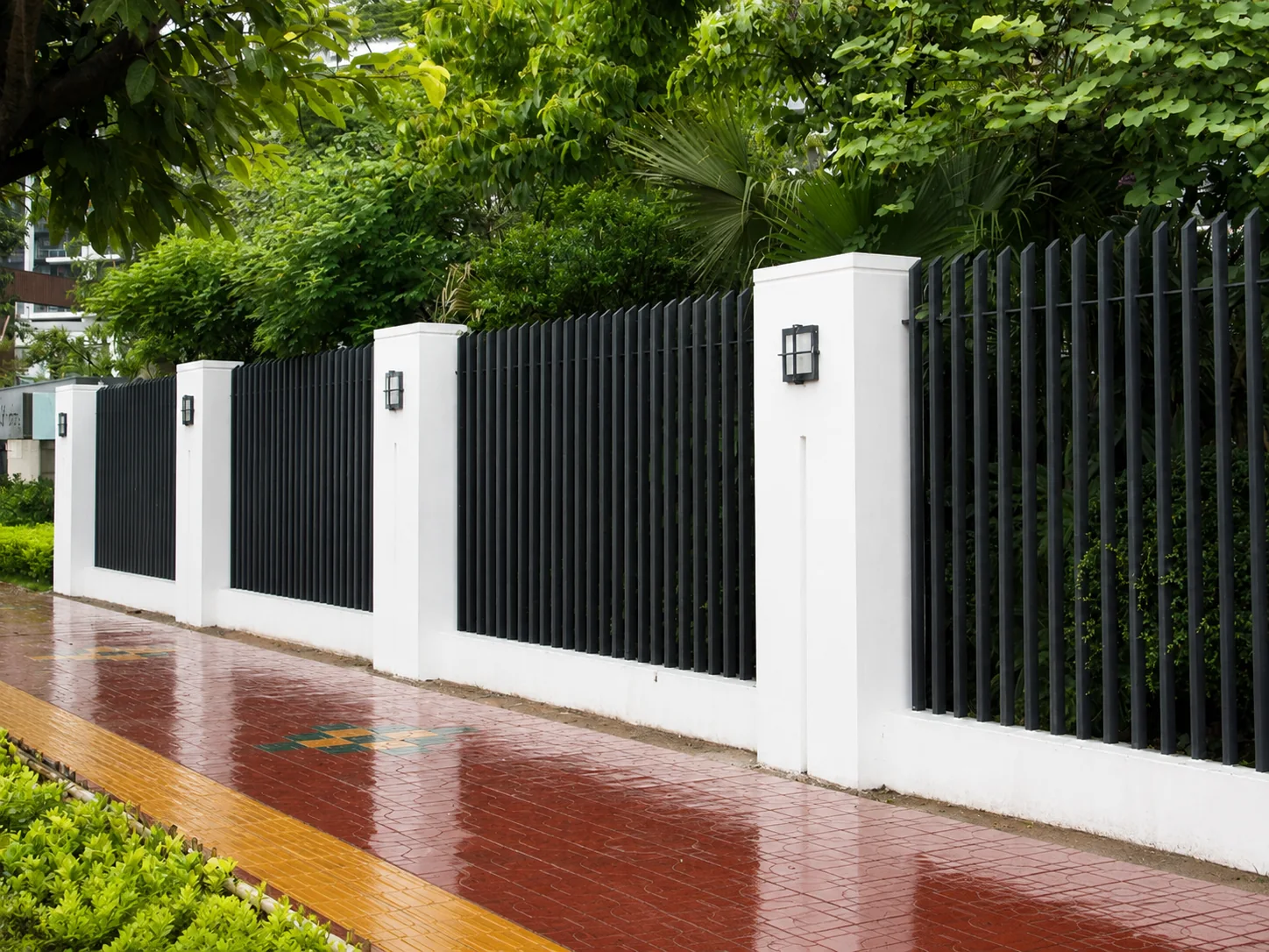 Black aluminium blade fence panels installed between white masonry pillars