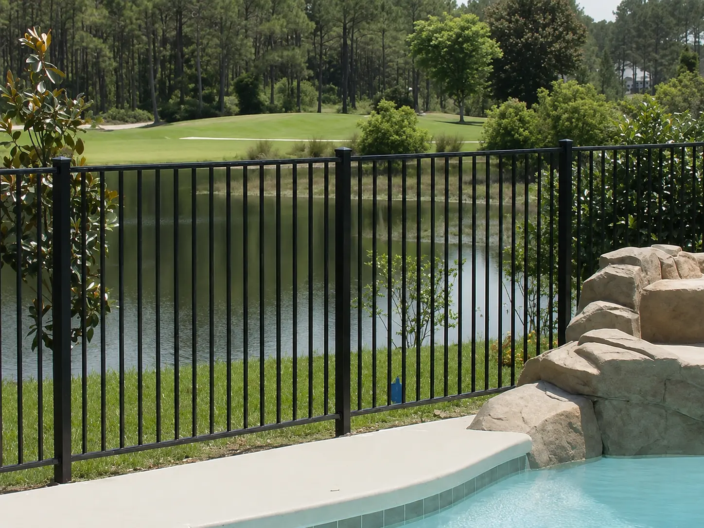 Black flat top steel fence installed beside a pool with a landscaped lake beyond