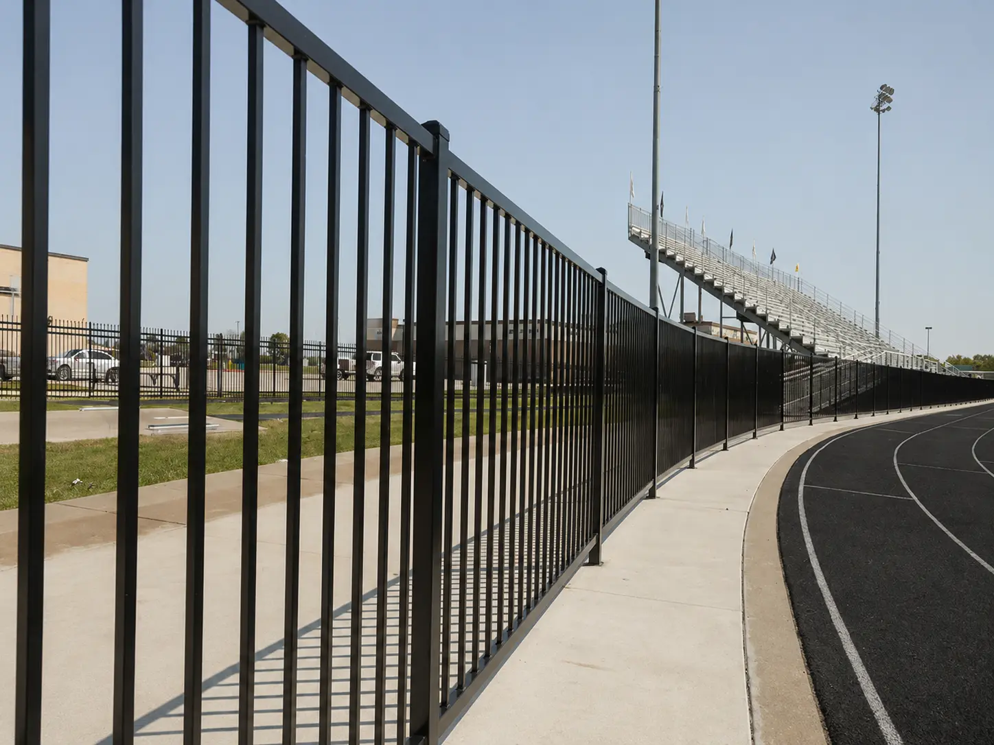 Black flat top steel fence installed along a sports facility track perimeter