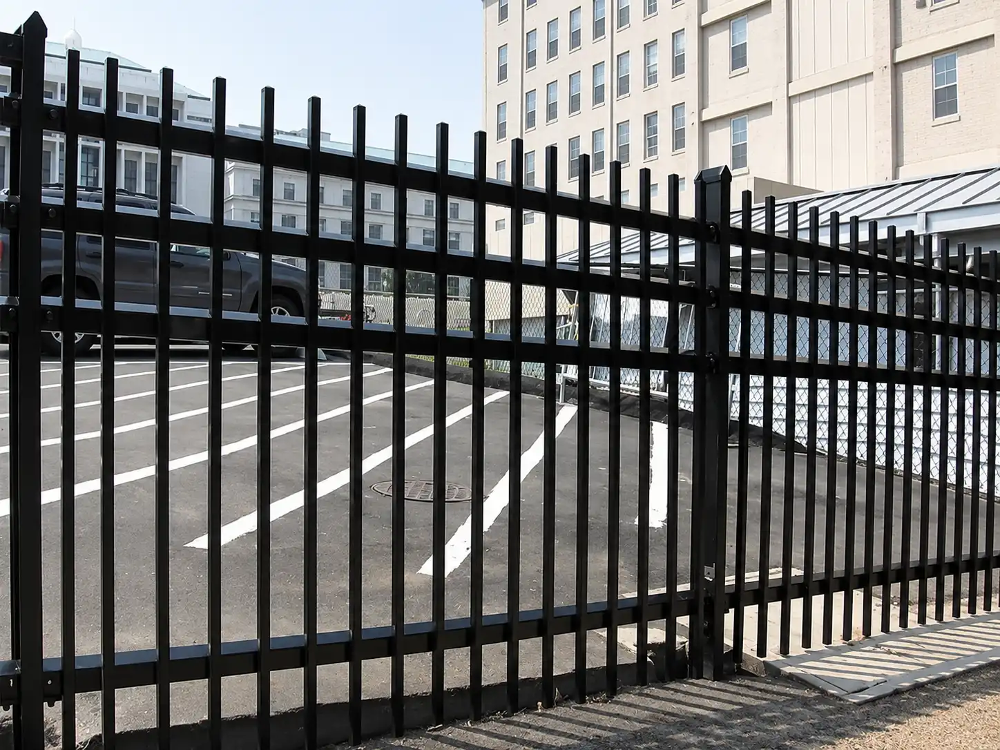 Black flat top steel rod fence and gate enclosing a commercial parking lot