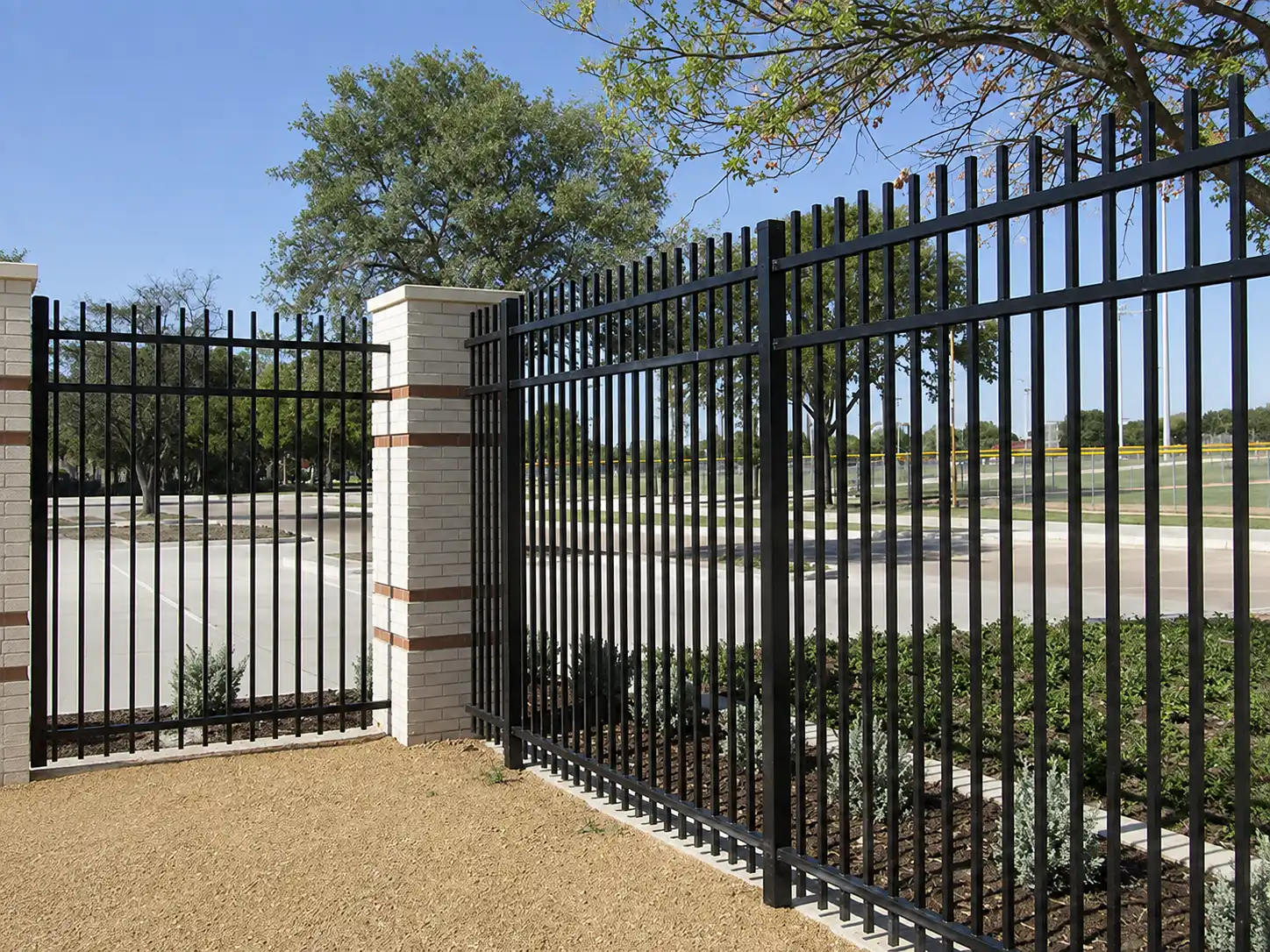 Black steel rod fence panels installed beside landscaping and a sports field