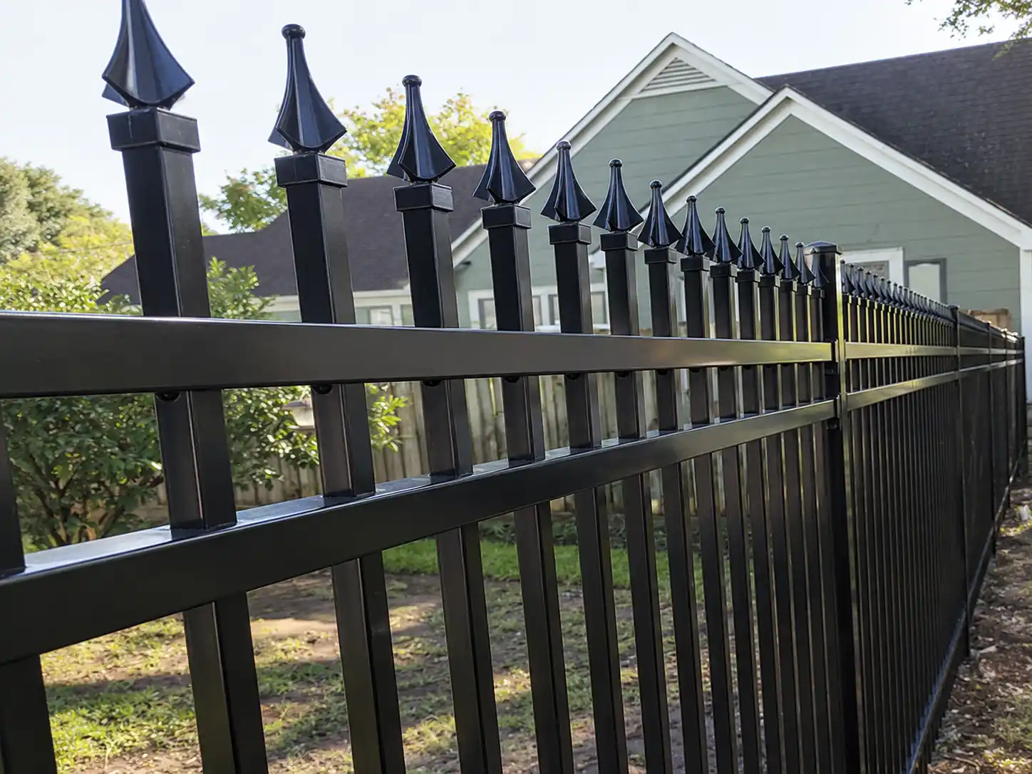 Close-up of black steel spear top fence pickets and three horizontal rails beside a house