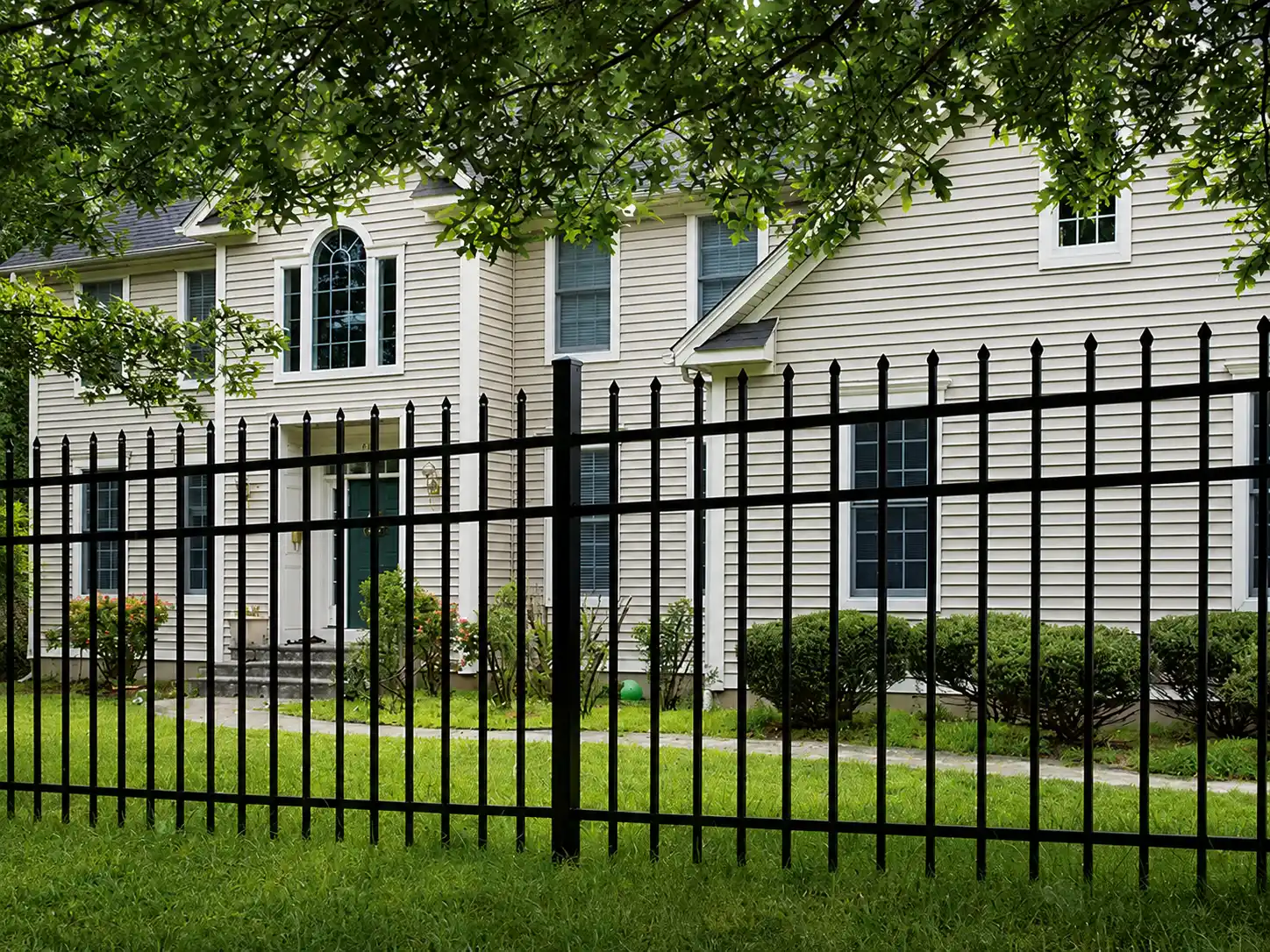 Black steel spear top fence with three horizontal rails installed across a landscaped front yard
