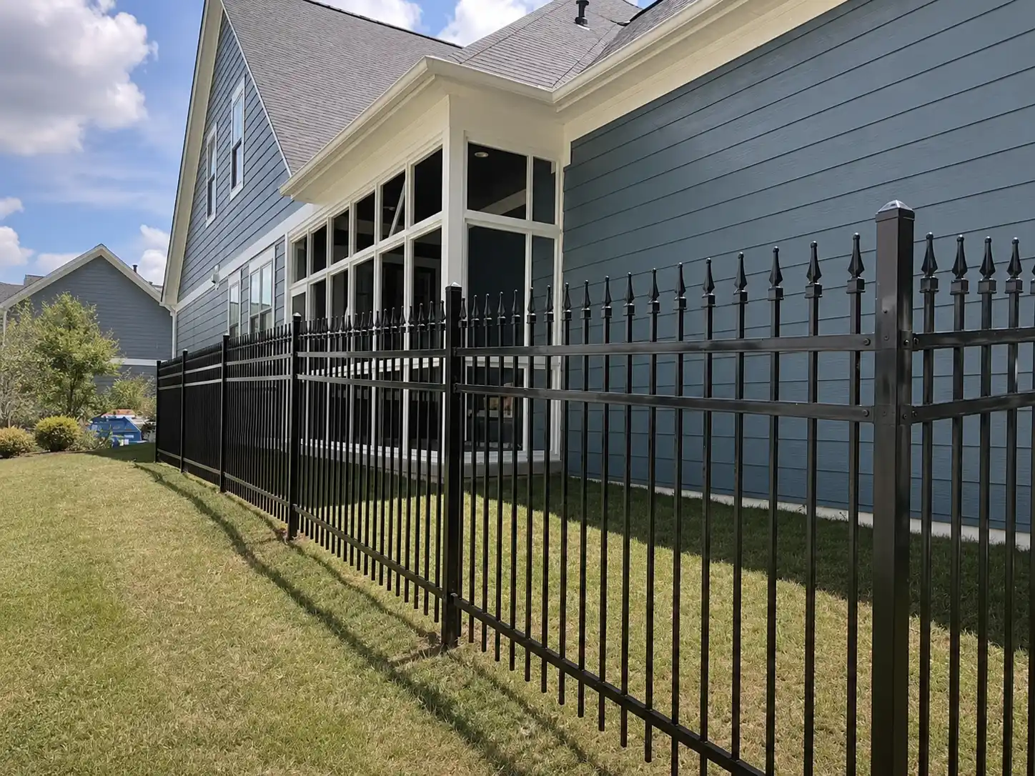 Black steel spear top fence with three horizontal rails installed along the side yard of a blue house