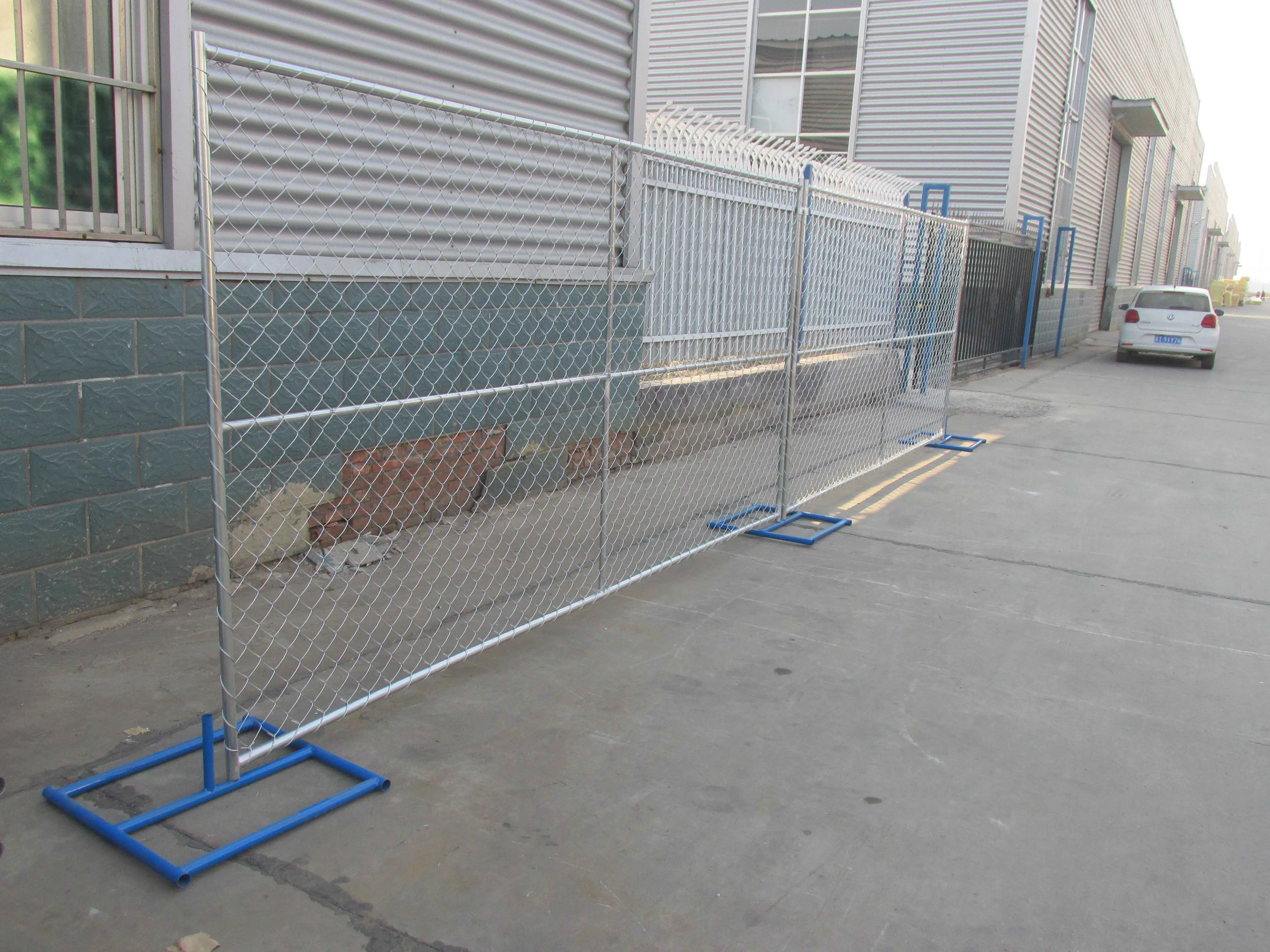 Temporary chain link fence panels installed with blue tubular steel feet beside a factory building